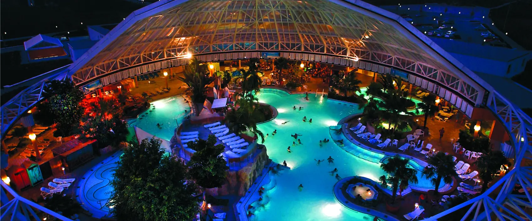 Glaskuppel der Therme Erding am Abend, darunter Becken und Palmen