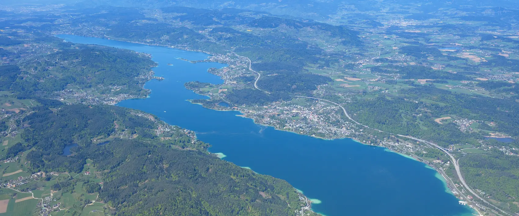 Wörthersee aus der Luft mit türkisem Wasser vor den Karawanken